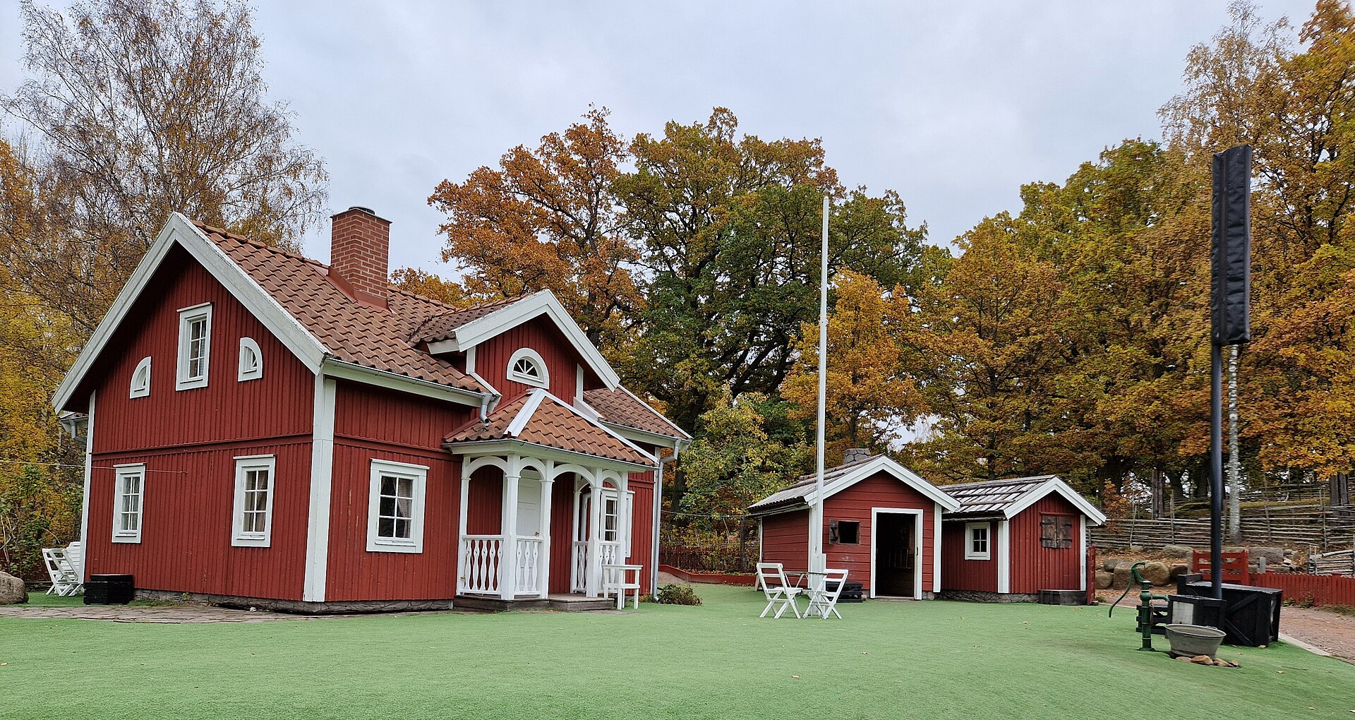 Astrid Lindgrens Welt in Vimmerby: das rote Wohnhaus von Katthult mit weißen Ecken, Fahnenstange und kleinen Nebengebäuden im Herbstlaub