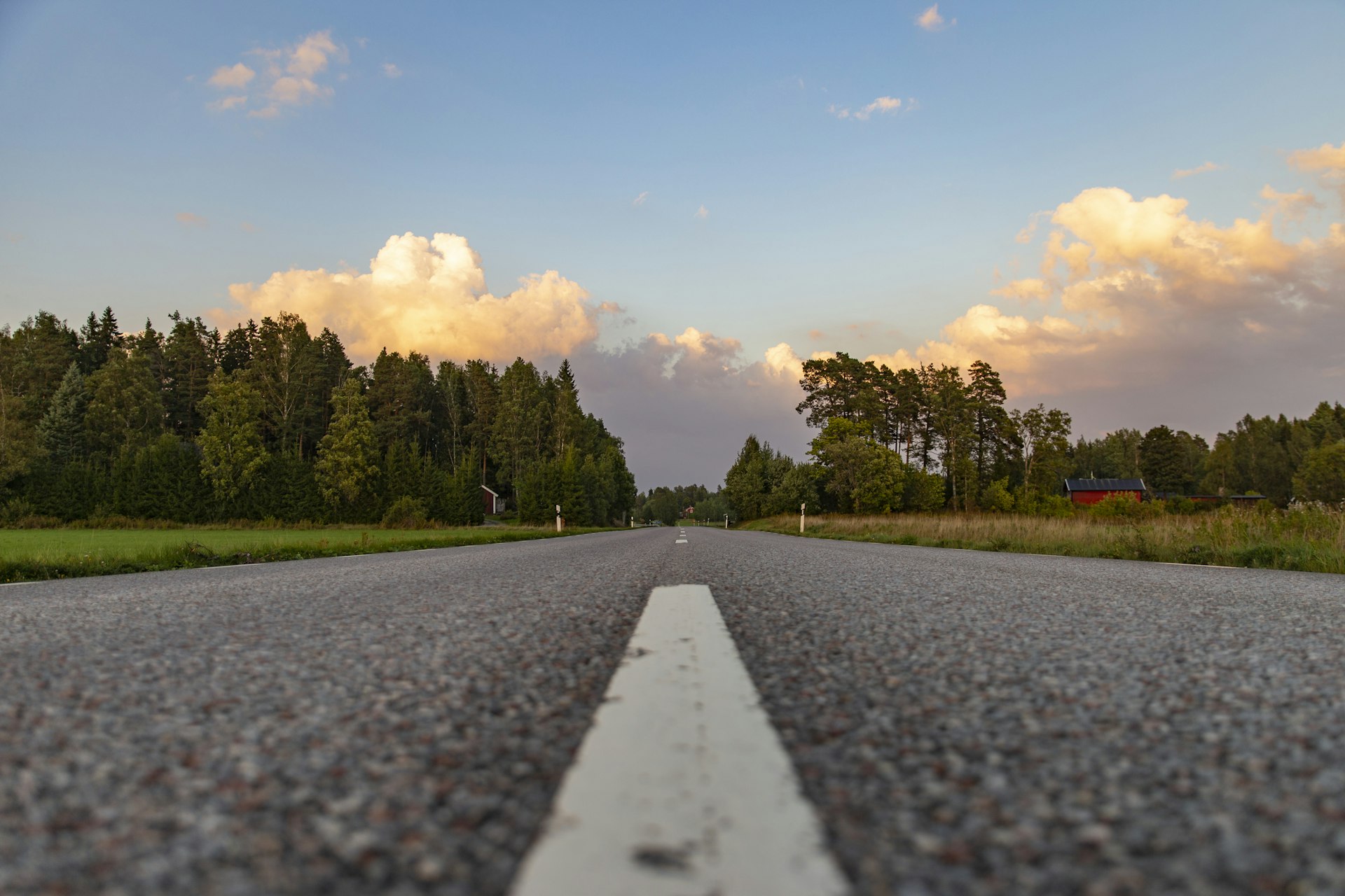 Autofahren in Schweden: leere Landstraße zwischen Wald und rotem Holzhaus bei Ervalla