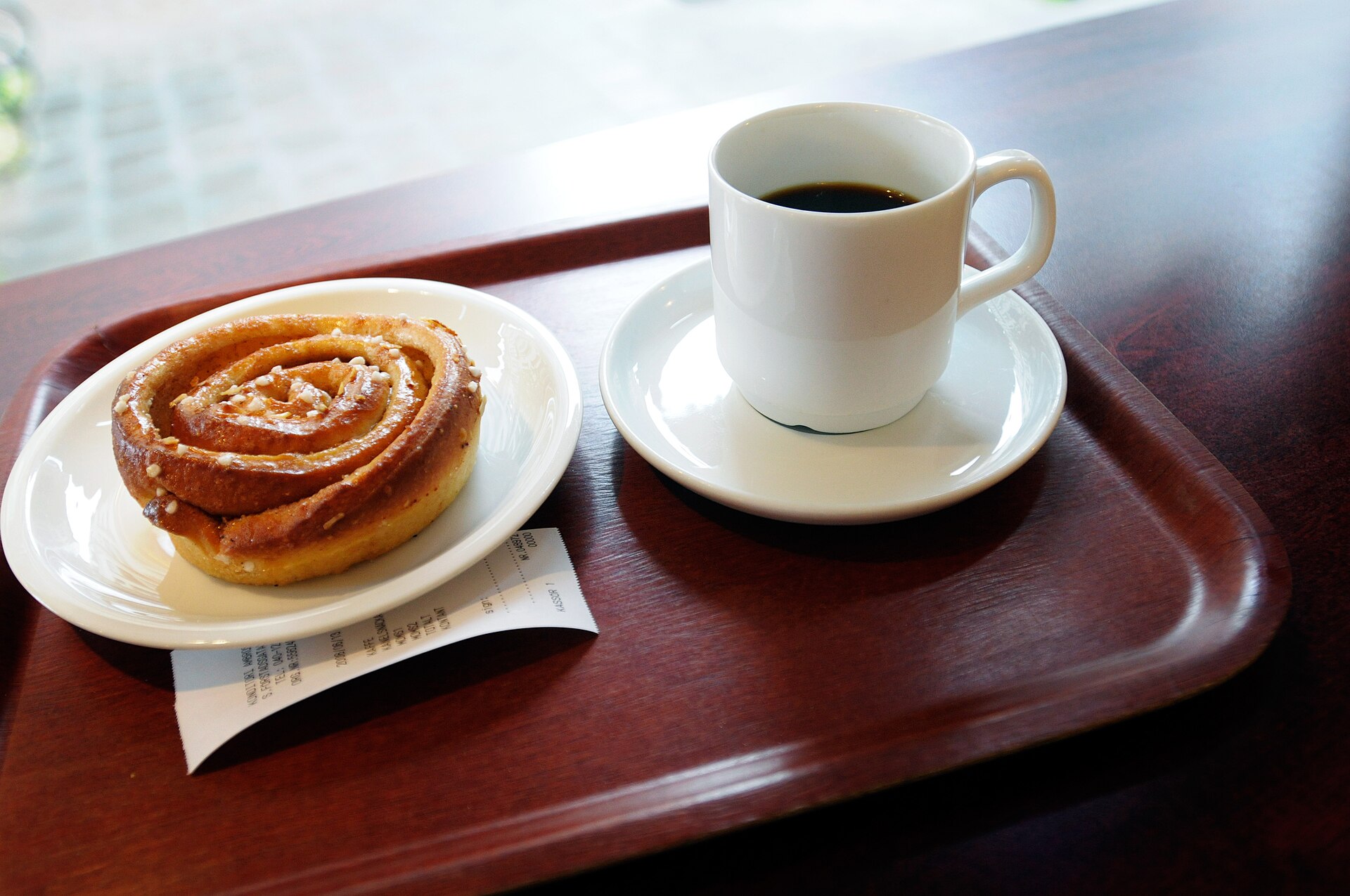 Fika in Schweden: Kanelbulle mit Perlzucker und eine Tasse schwarzer Filterkaffee auf einem Tablett