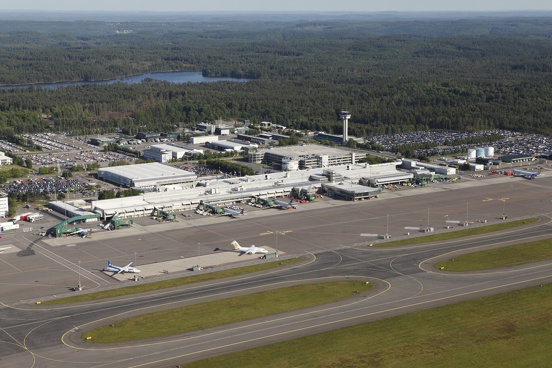 Flug nach Schweden: der Flughafen Göteborg-Landvetter aus der Luft mit Terminal, Tower und Vorfeld, umgeben von Wald und einem See