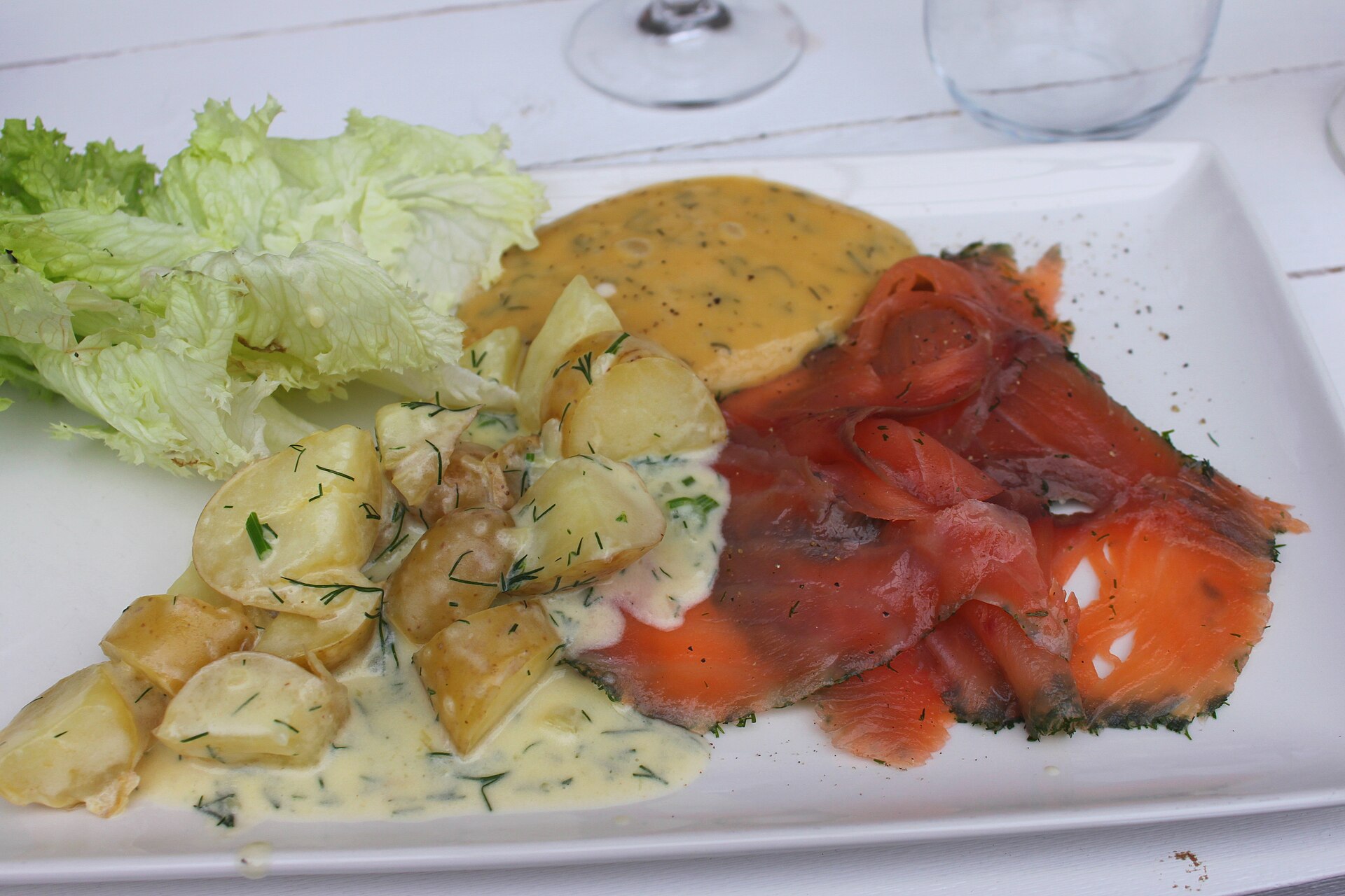 Graved Lachs mit Senf-Dill-Soße und Dillkartoffeln auf einem weißen Teller