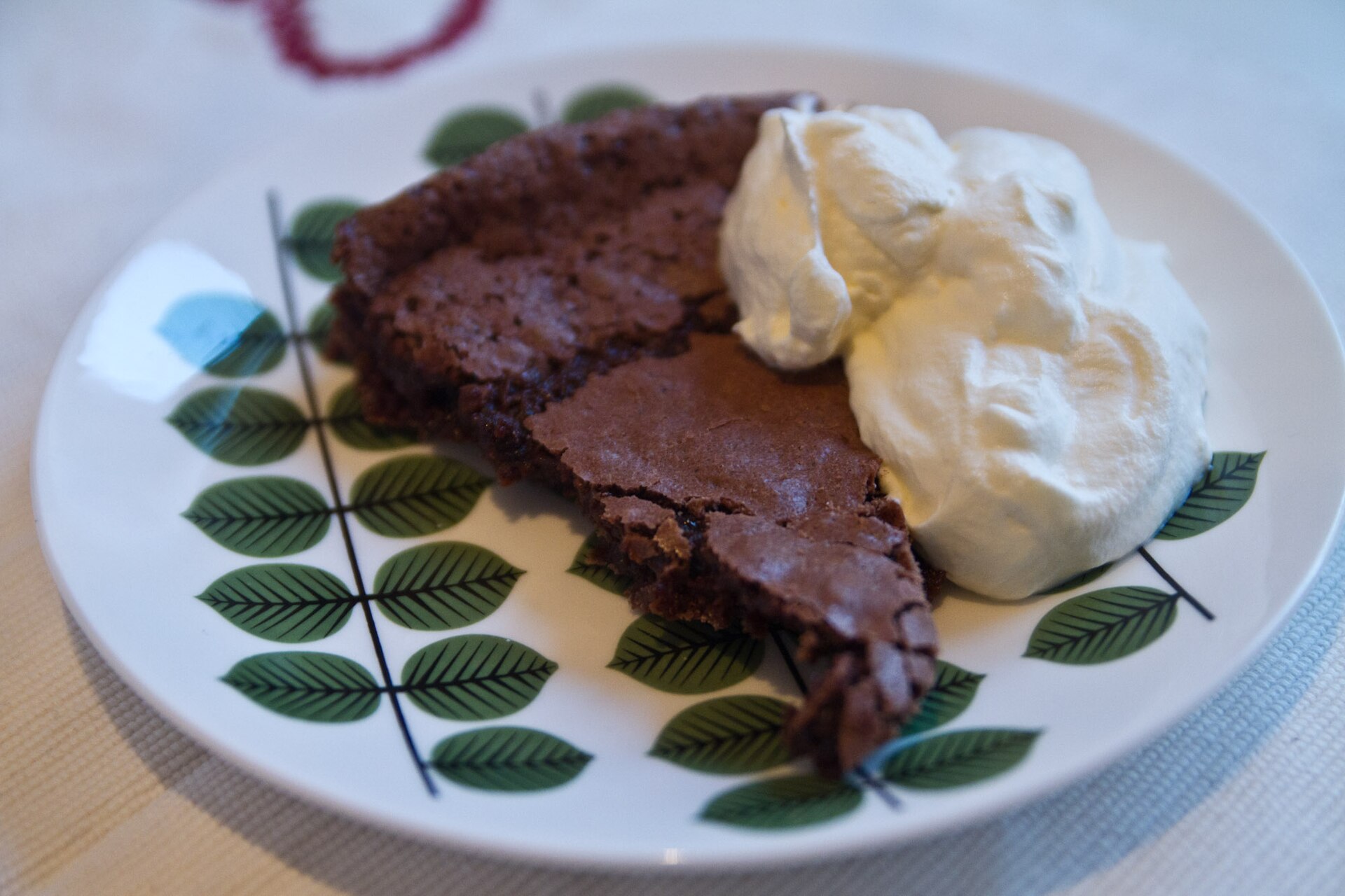 Kladdkaka: ein Stück schwedischer Schokoladenkuchen mit klebriger Mitte und Schlagsahne auf einem Teller mit Blattmuster
