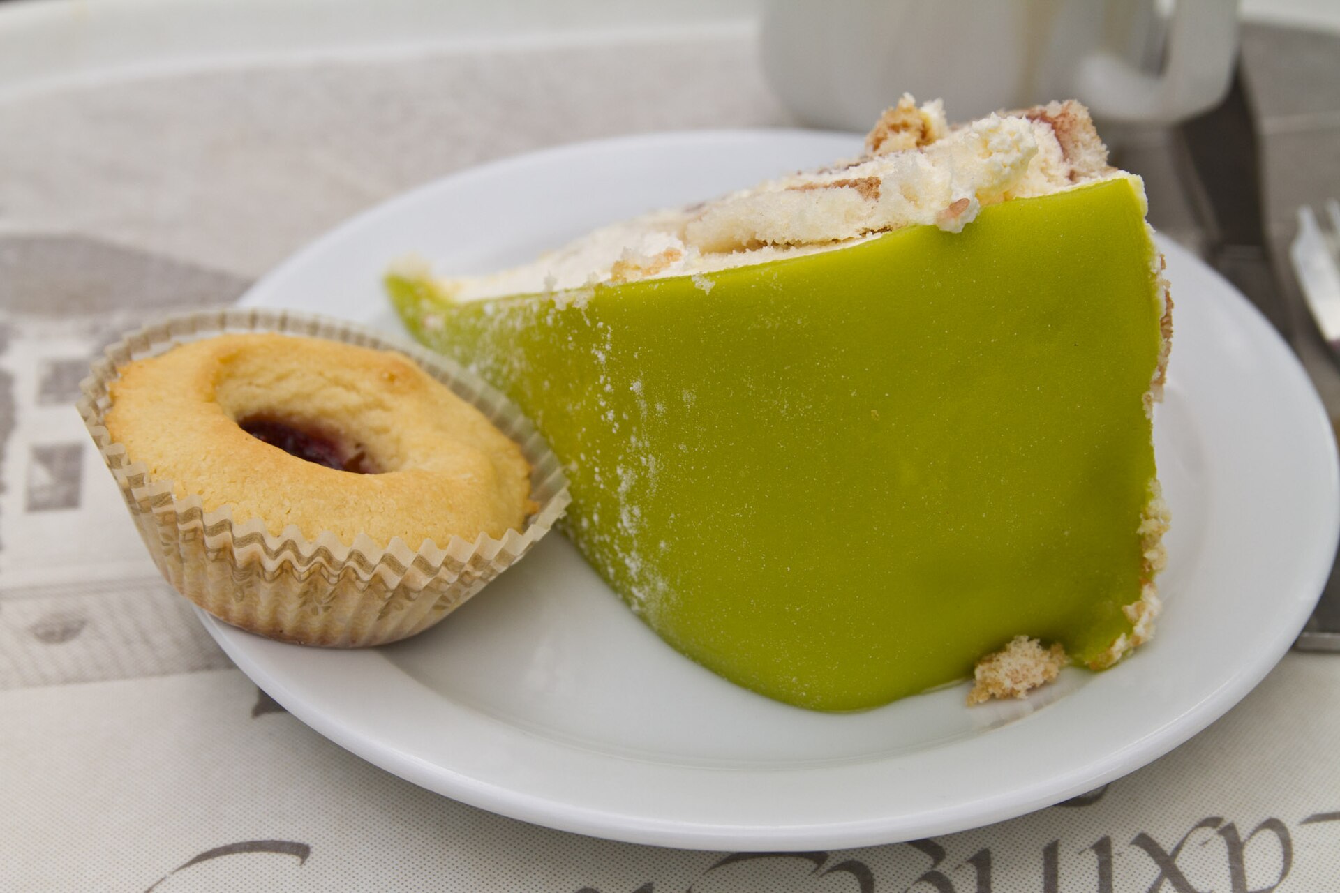 Prinsesstårta: ein Stück schwedische Torte mit grünem Marzipan, Sahne und Biskuit, daneben eine Hallongrotta auf einem weißen Teller