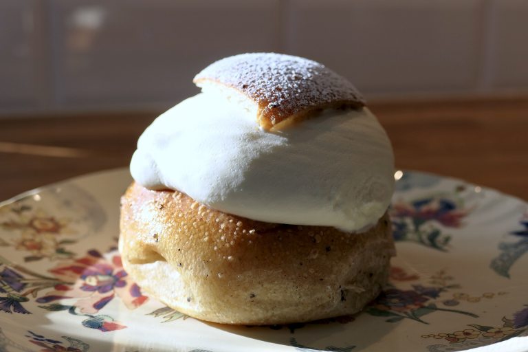 Semla mit dreieckigem Deckel, Schlagsahne und Puderzucker auf einem geblümten Porzellanteller
