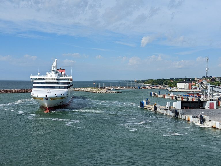 Die weiße Gotlandfähre M/S Visby fährt aus dem Hafen von Visby, rechts die Kaianlagen, im Hintergrund die Ostsee