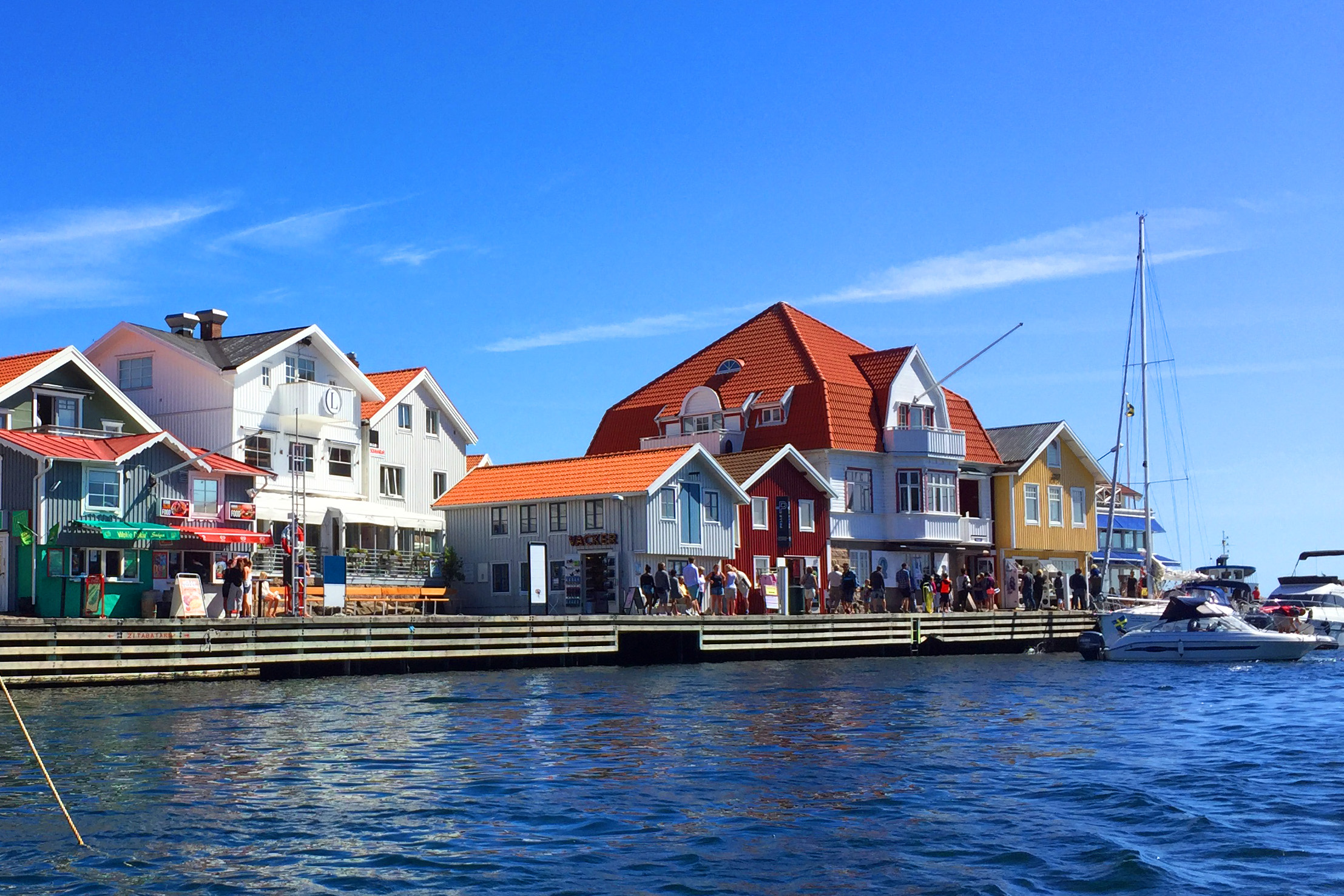 Ferienhaus in Schweden am Meer: bunte Holzhäuser direkt am Wasser an der Smögenbryggan in Bohuslän, davor Boote