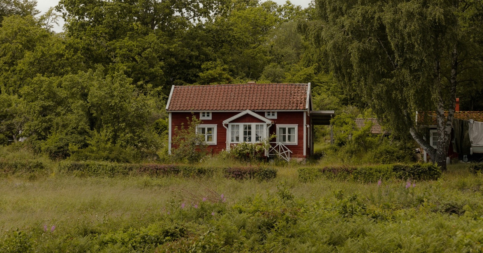 Ferienhaus in Schweden: rotes Holzhaus zwischen Wiese und Laubbäumen