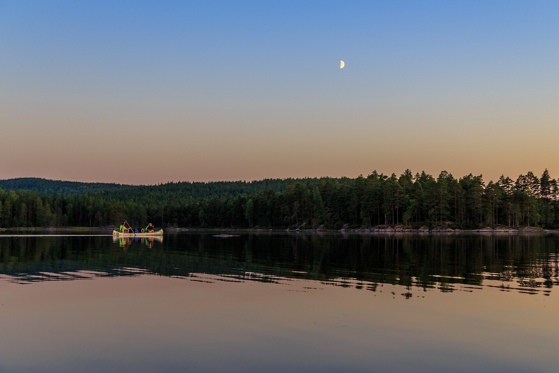 Kanutour in Schweden: Kanadier mit zwei Paddlern auf dem spiegelglatten See Stora Gla im Naturreservat Glaskogen in Värmland, Abendhimmel mit Halbmond über dem Nadelwald