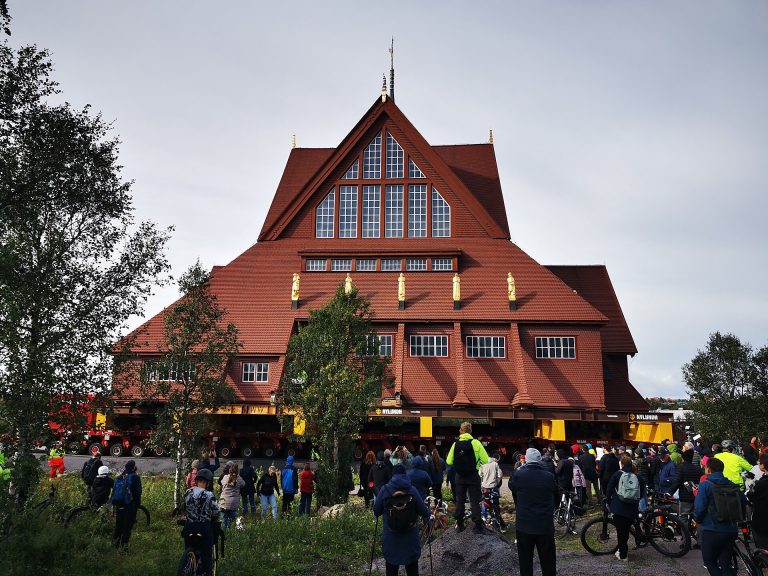 Kiruna kyrka wird im August 2025 auf Schwerlastfahrzeugen an ihren neuen Platz in Kiruna gefahren, davor Zuschauer