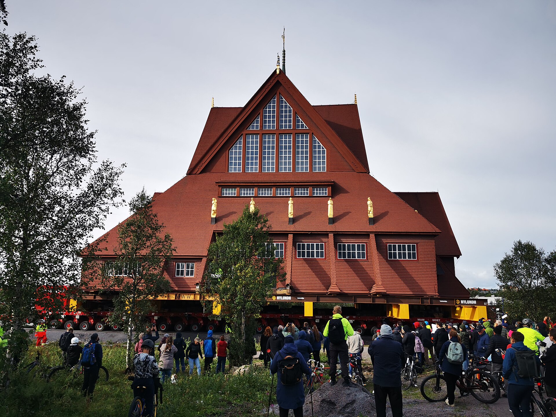 Kiruna kyrka wird im August 2025 auf Schwerlastfahrzeugen an ihren neuen Platz in Kiruna gefahren, davor Zuschauer