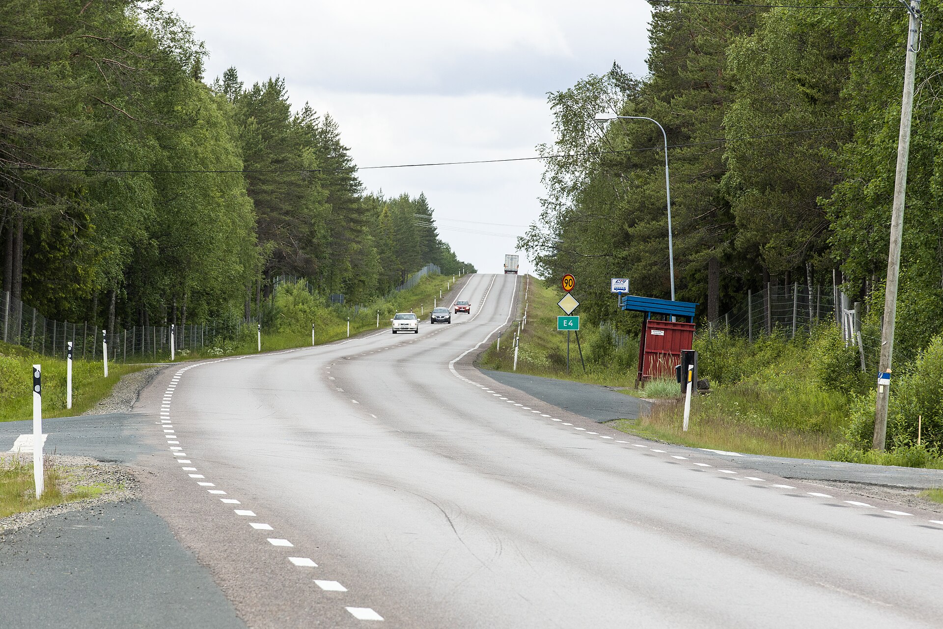 Mietwagen in Schweden: drei Autos und ein Lkw auf der E4 zwischen Sangis und Haparanda, am Rand Wildzäune, ein Schild mit Tempo 90 und eine rote Wartehalle