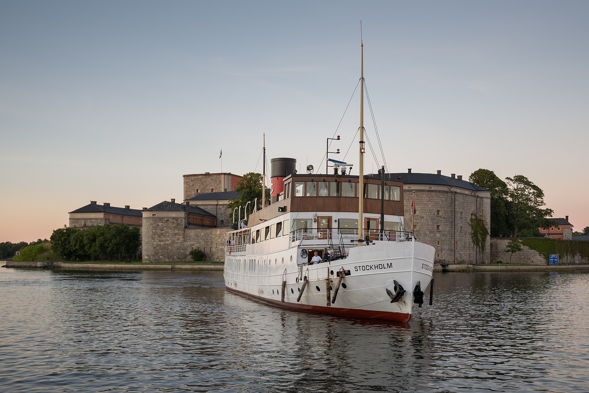 Schärenrundfahrt in Stockholm: das weiße Dampfschiff S/S Stockholm mit rotem Schornstein vor der Festung Vaxholm im Abendlicht