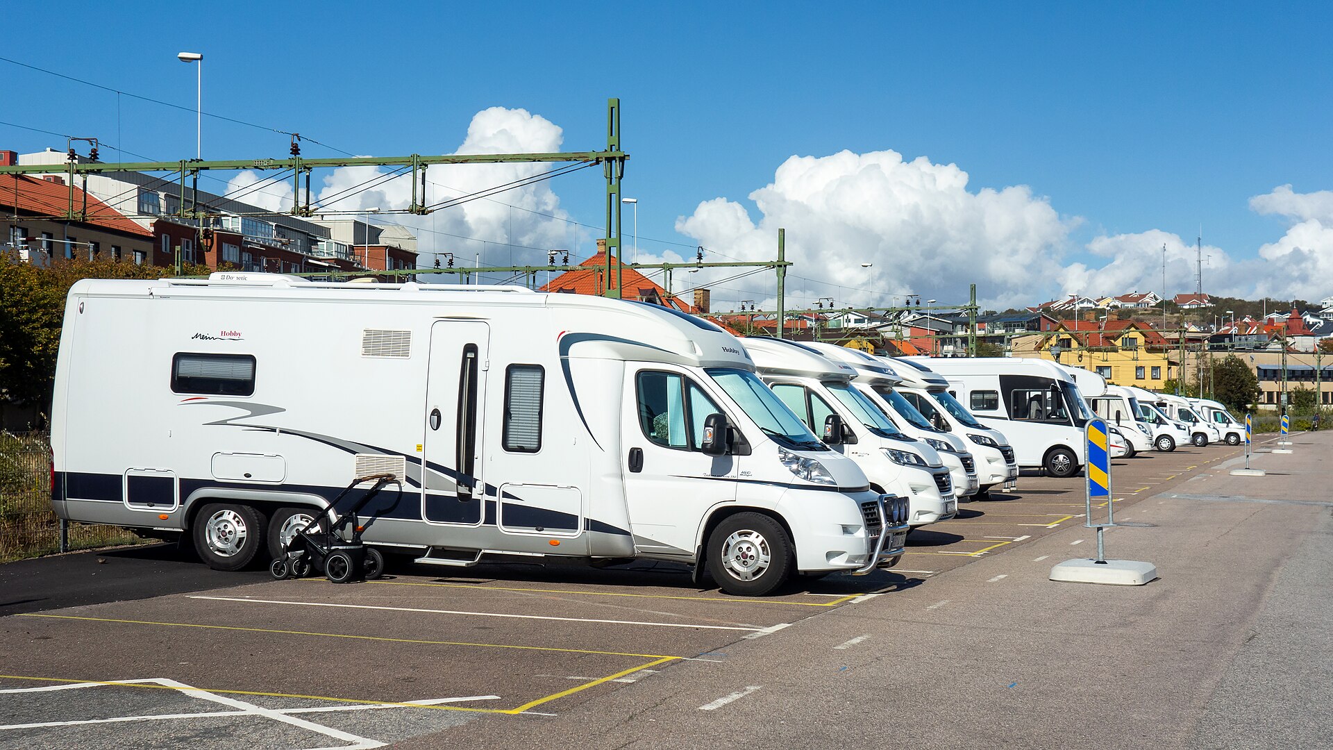 Mit dem Wohnmobil nach Schweden: weiße Wohnmobile in einer Reihe auf dem Stellplatz am Hafen von Lysekil, dahinter Häuser mit roten Dächern unter blauem Himmel