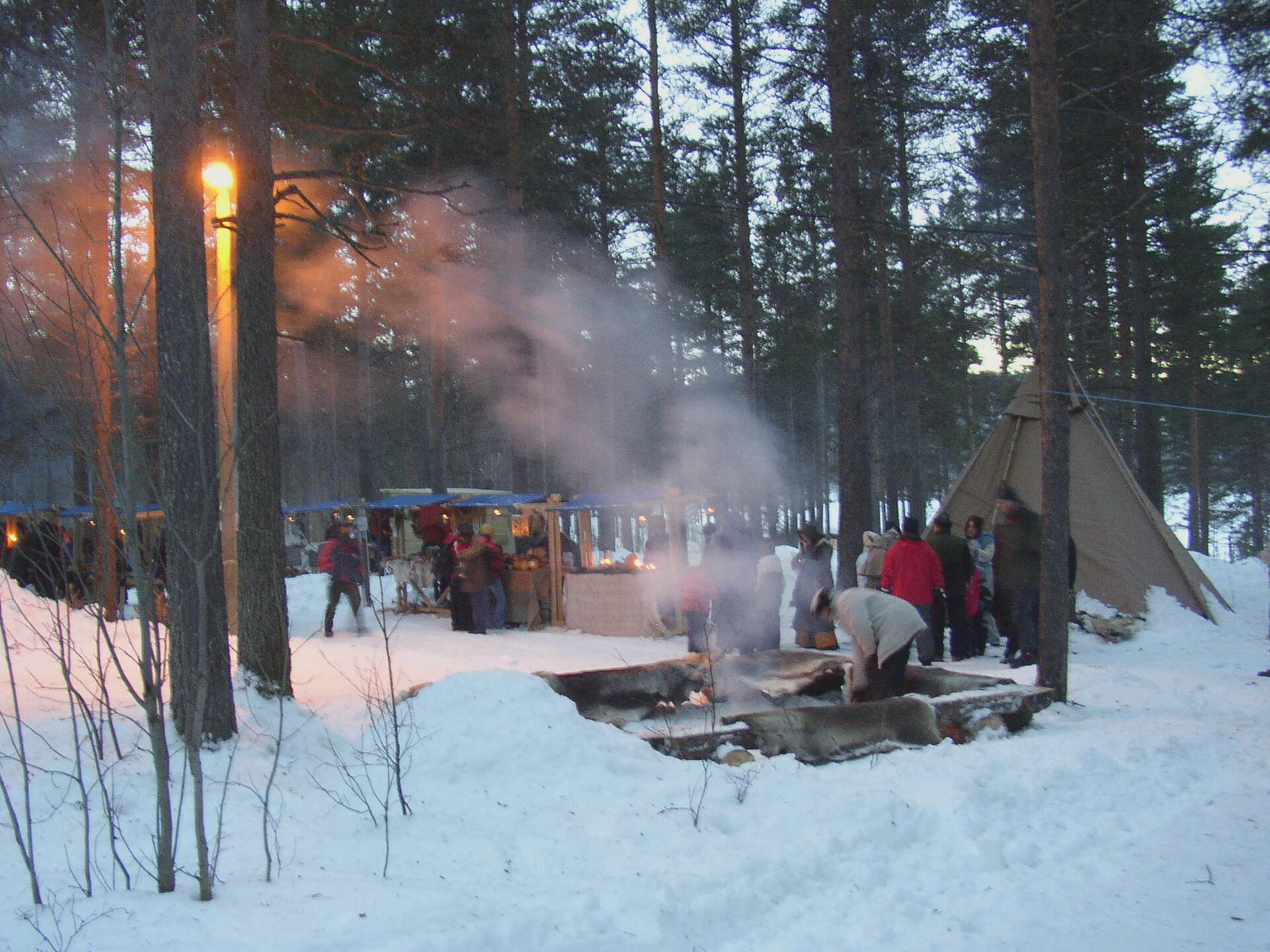 Winterlicher Markt in Jokkmokk mit Ständen, Lavvu-Zelt und Rauch im Schnee
