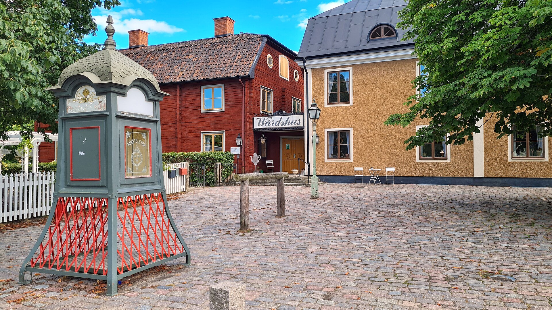 Kopfsteinpflasterplatz in Gamla Linköping mit roten Holzhäusern und altem Telefonkiosk