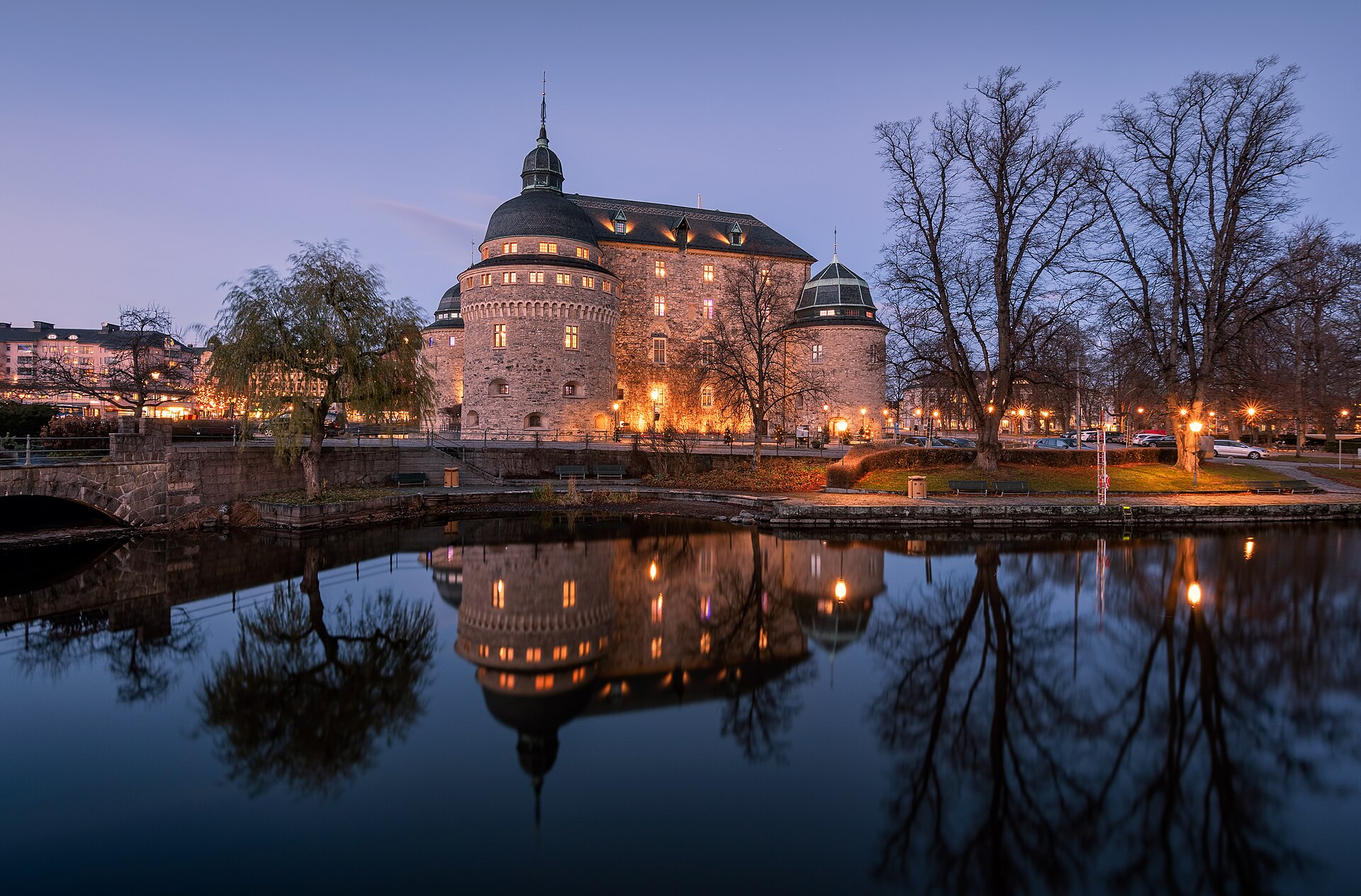 Das beleuchtete Schloss Örebro in der Abenddämmerung, gespiegelt im Wasser des Svartån