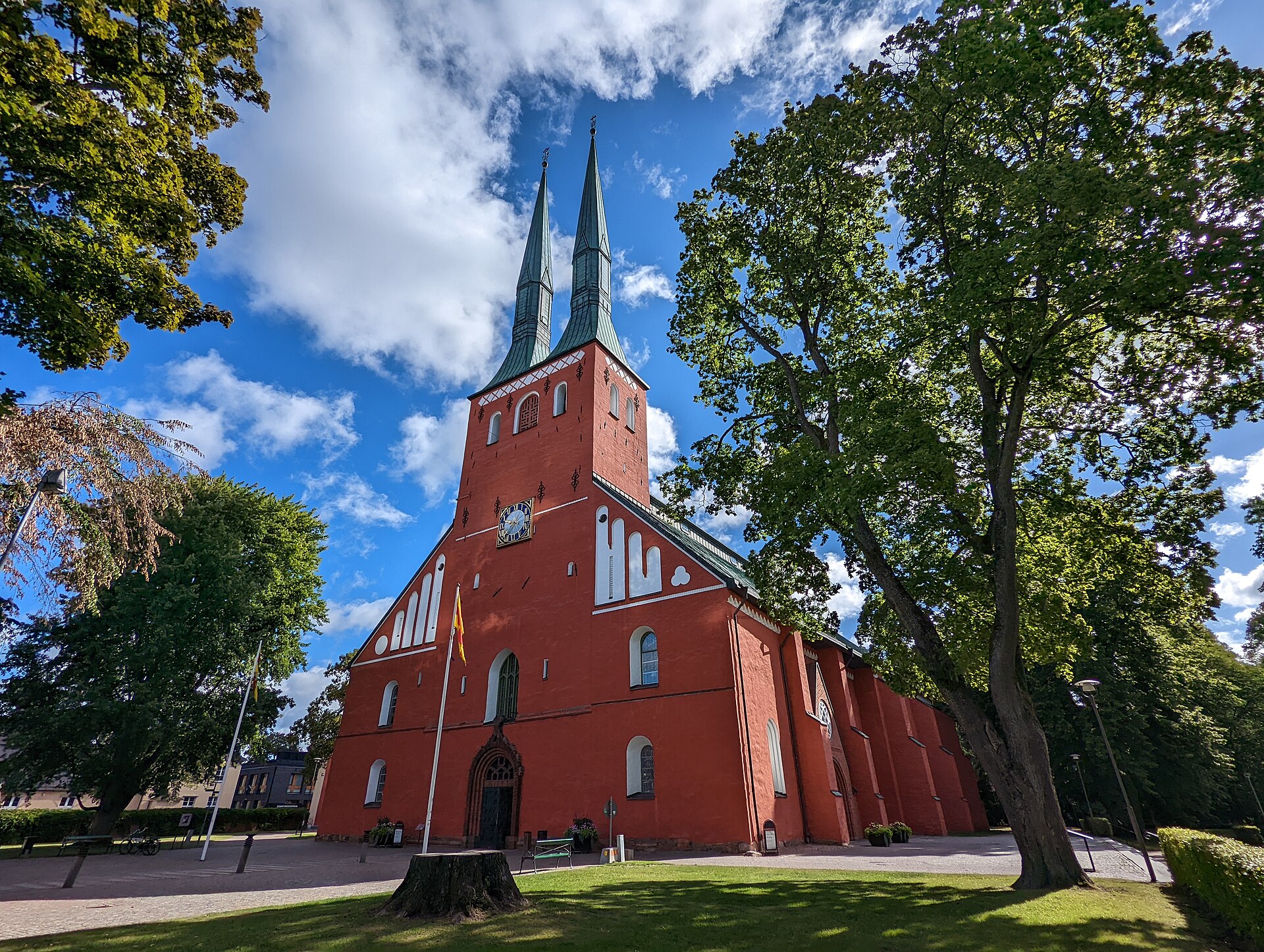 Die rote Domkirche von Växjö mit zwei grünen Turmspitzen unter blauem Himmel